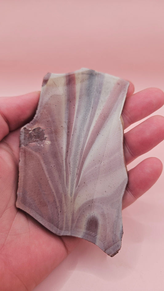 Fanburst-pattern rhyolite slab with radiating mauve and cream bands, 73 grams and 3.8x2.3 inches, cut and smoothed for display or lapidary work.