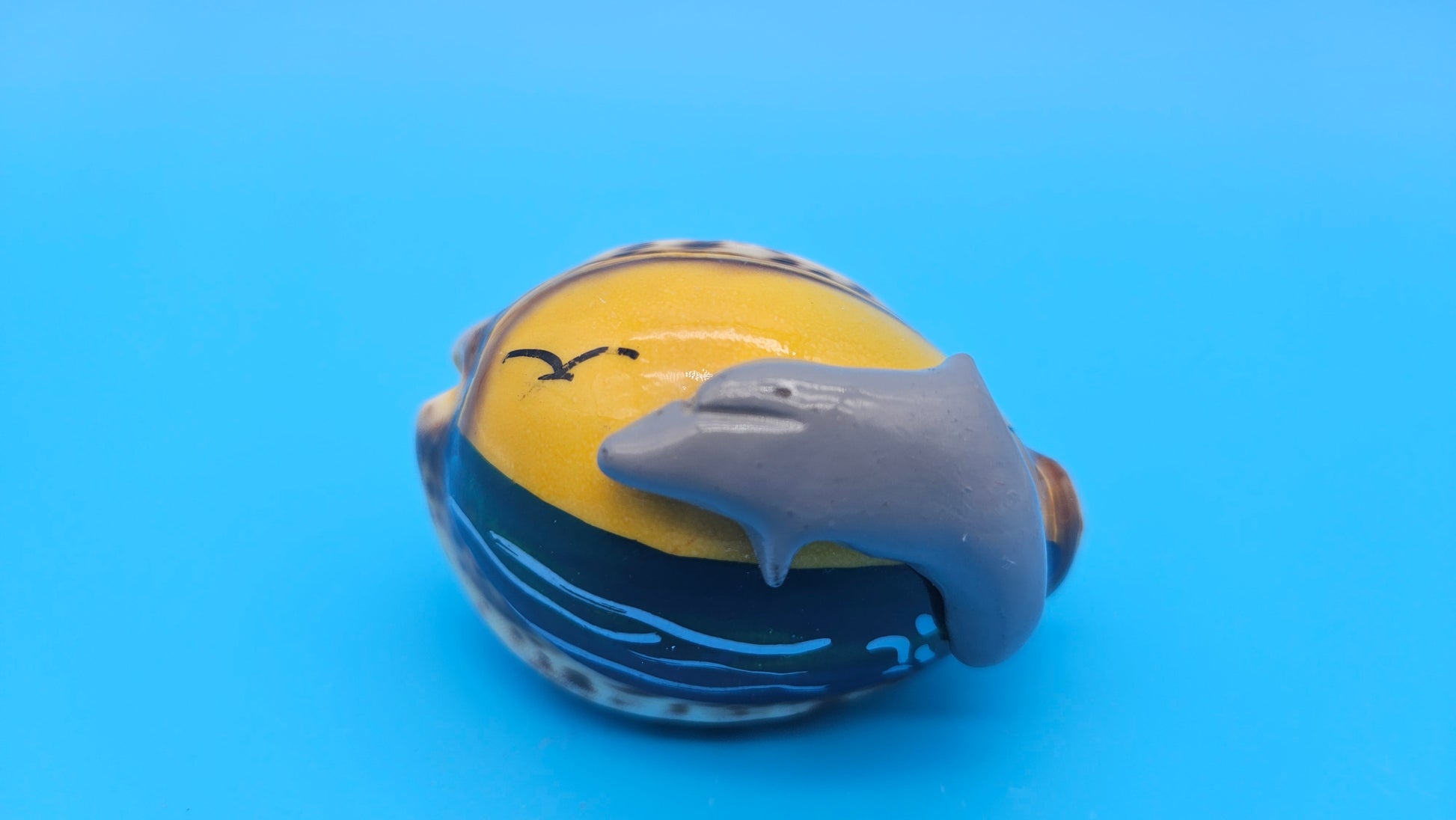 Painted cowrie shell magnet with dolphin leaping across yellow sunset scene