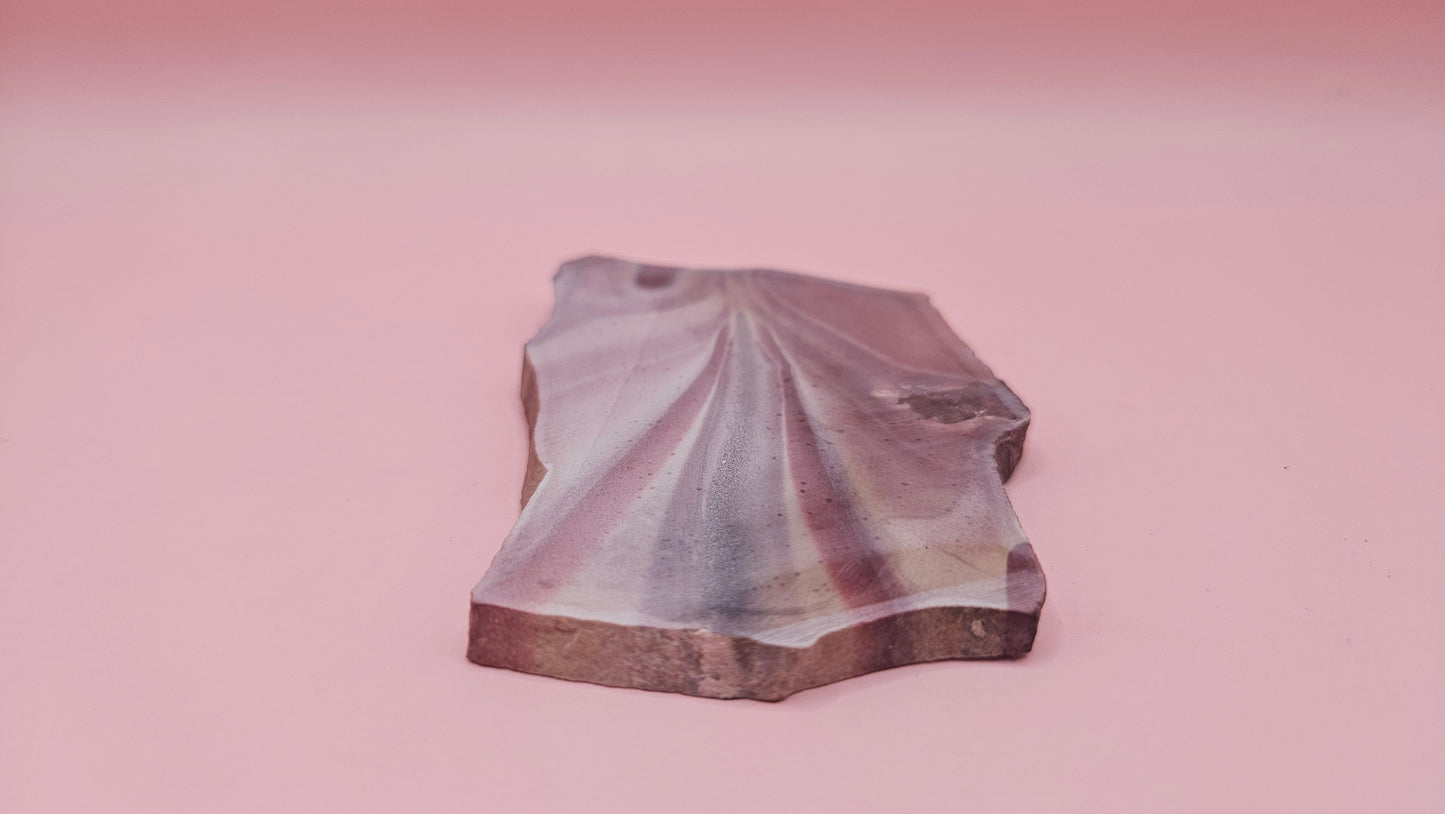 Fanburst-pattern rhyolite slab with radiating mauve and cream bands, 73 grams and 3.8x2.3 inches, cut and smoothed for display or lapidary work.