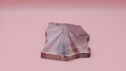 Fanburst-pattern rhyolite slab with radiating mauve and cream bands, 73 grams and 3.8x2.3 inches, cut and smoothed for display or lapidary work.