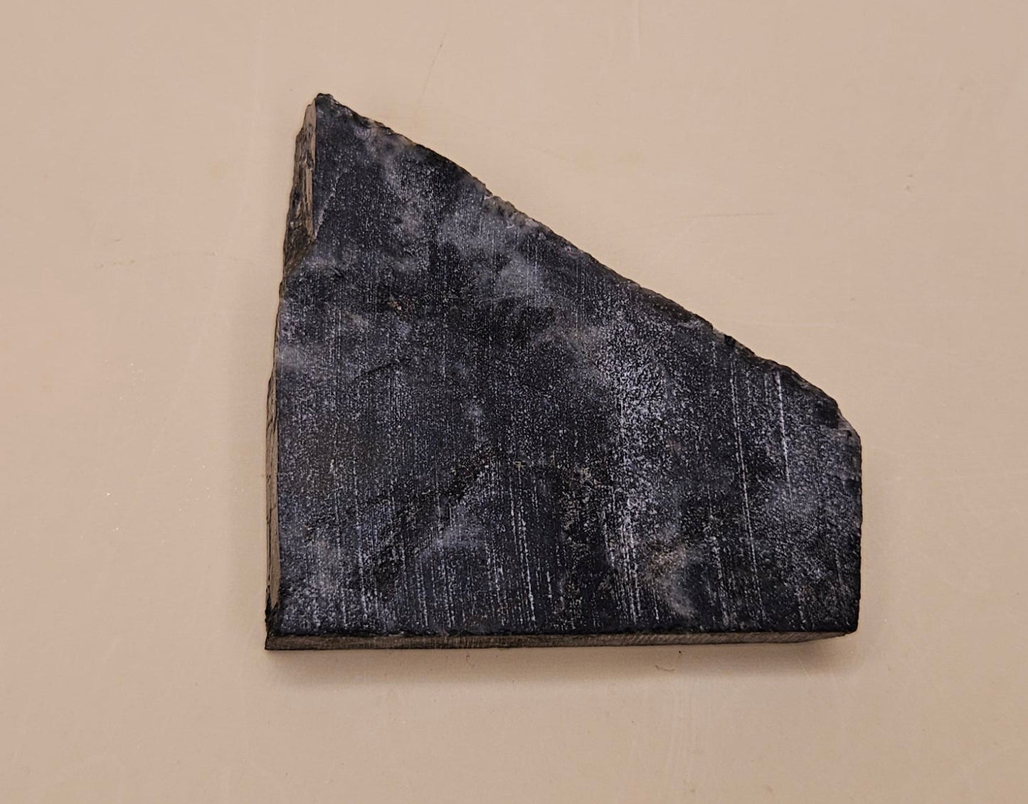 28g polished Spectrolite slab from Finland shown in hand with dark gray base and flashes of blue-green light.