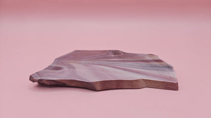 Fanburst-pattern rhyolite slab with radiating mauve and cream bands, 73 grams and 3.8x2.3 inches, cut and smoothed for display or lapidary work.
