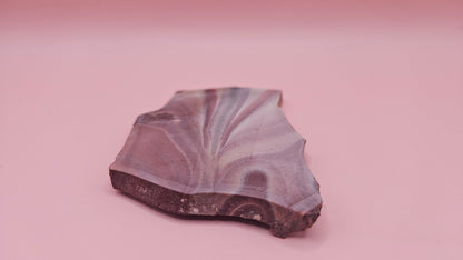 Fanburst-pattern rhyolite slab with radiating mauve and cream bands, 73 grams and 3.8x2.3 inches, cut and smoothed for display or lapidary work.