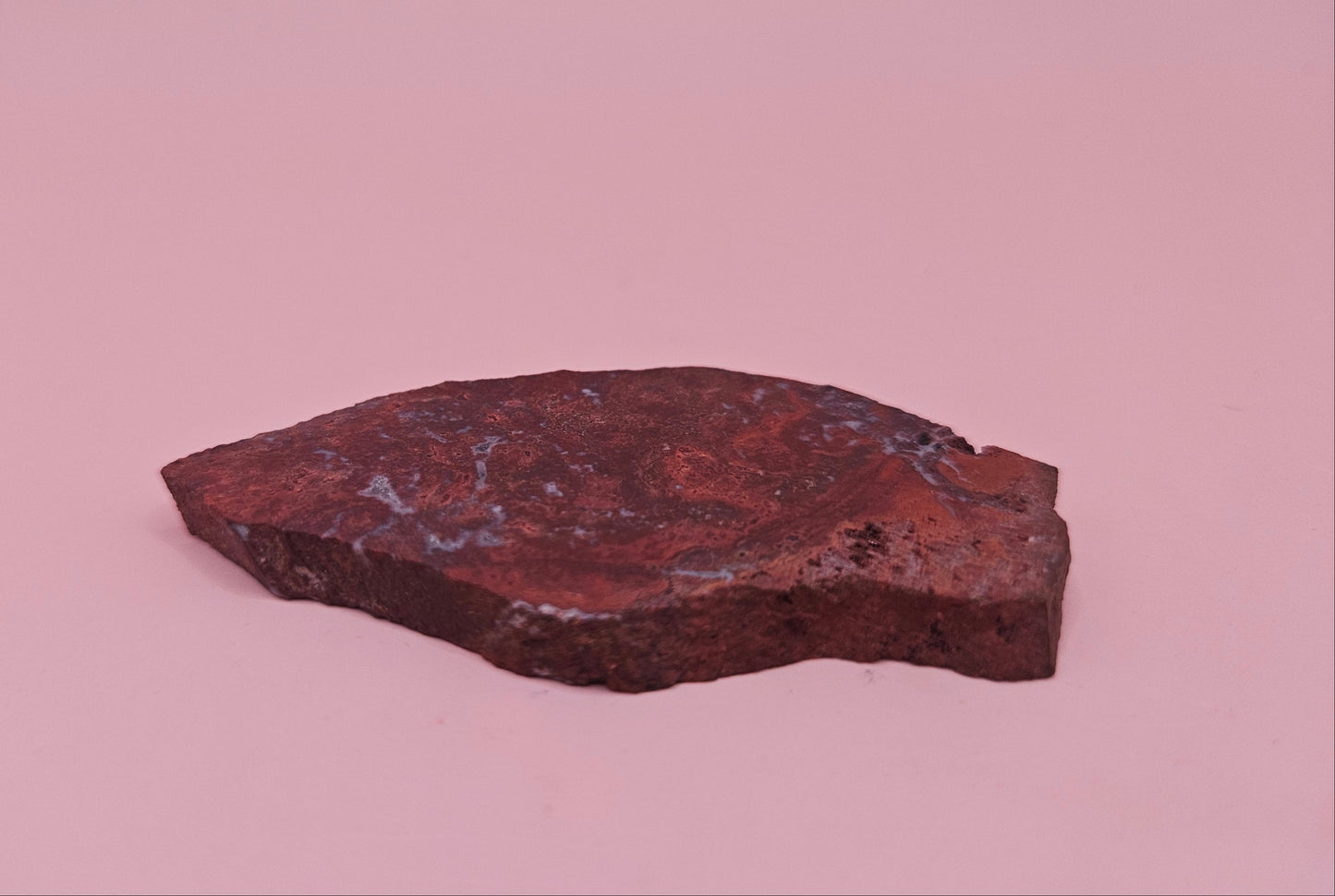 Moss Agate slab 22g, reddish with blue-white moss-like inclusions, 2.6x1.3 inches, photographed on pink background.