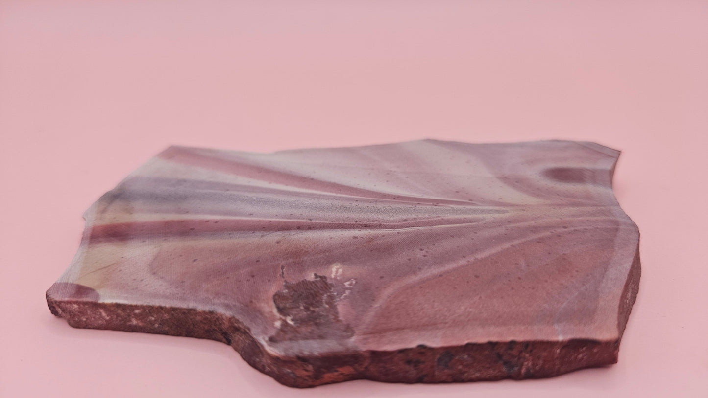 Fanburst-pattern rhyolite slab with radiating mauve and cream bands, 73 grams and 3.8x2.3 inches, cut and smoothed for display or lapidary work.