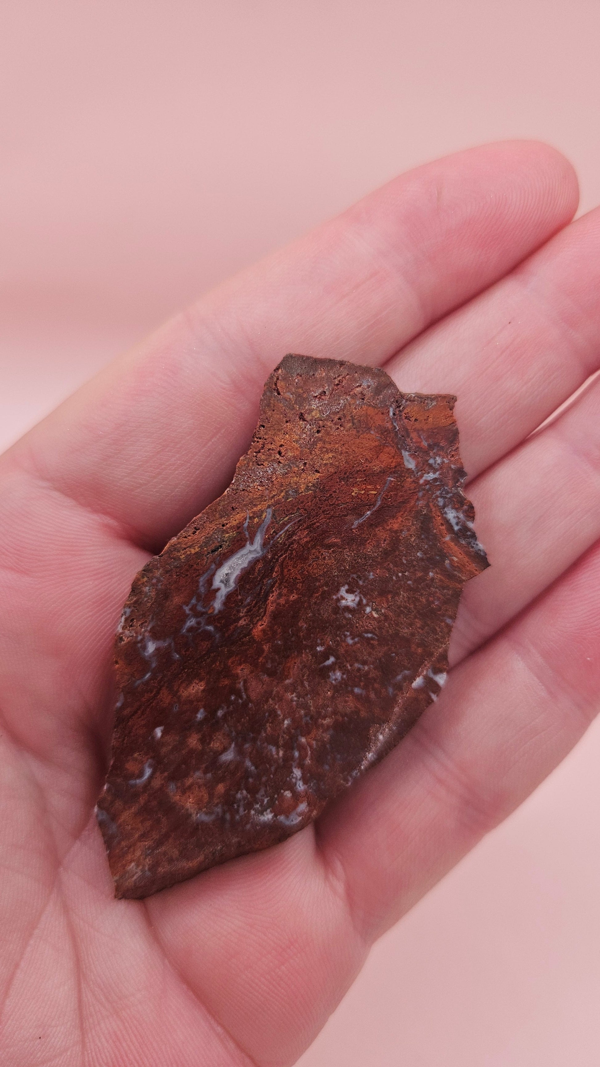 Moss Agate slab 22g, reddish with blue-white moss-like inclusions, 2.6x1.3 inches, photographed on pink background.