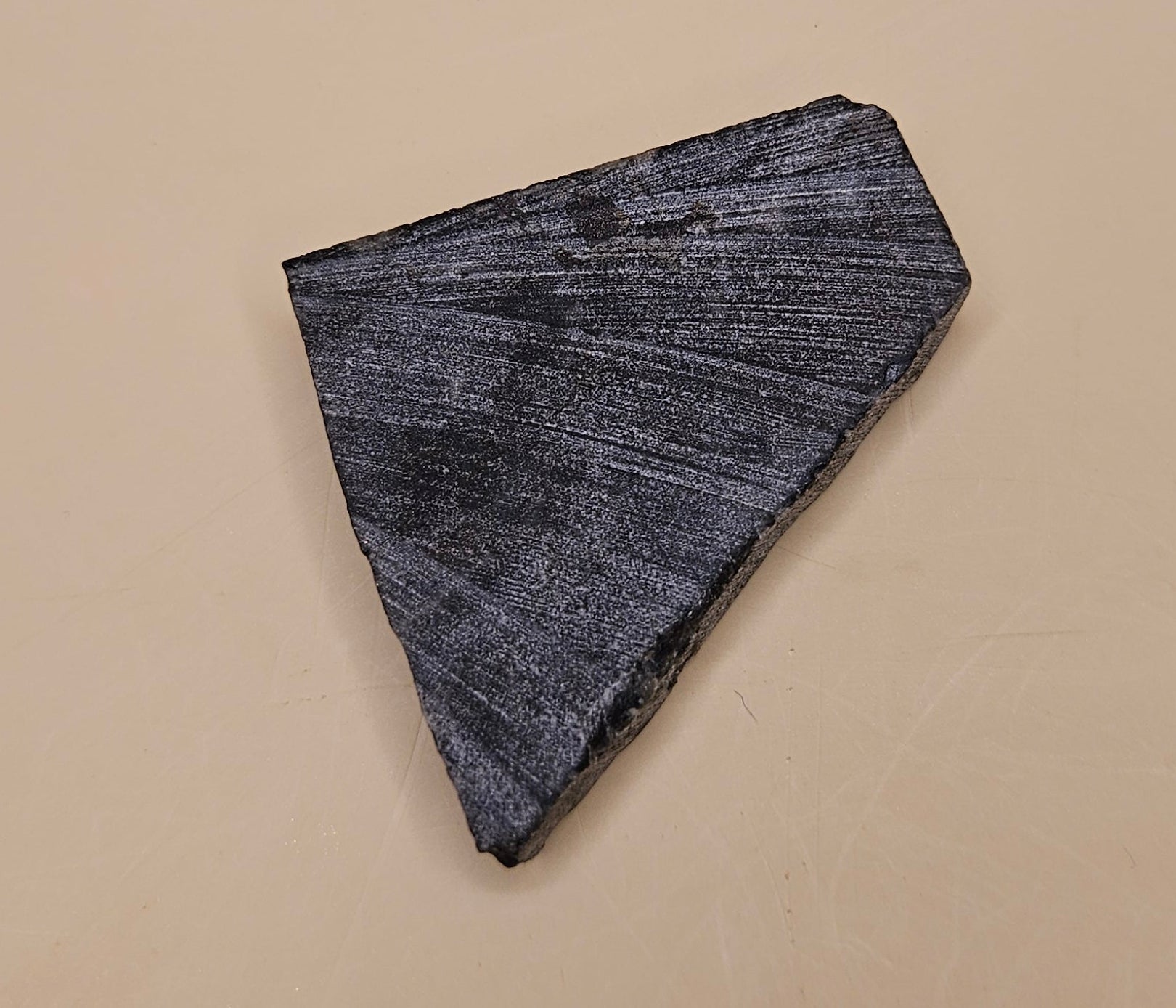 28g polished Spectrolite slab from Finland shown in hand with dark gray base and flashes of blue-green light.